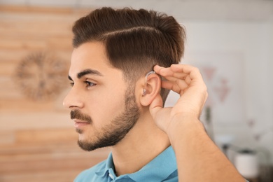 Young man adjusting hearing aid at home