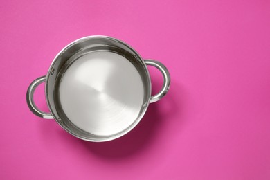 Empty steel pot on dark pink background, top view. Space for text