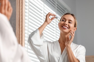 Photo of Beautiful woman applying cosmetic serum onto her face near mirror in bathroom