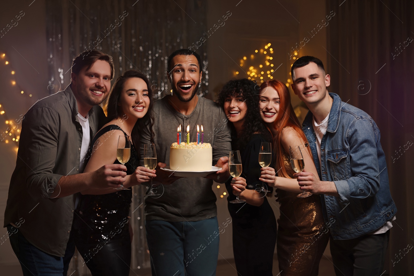 Photo of Happy friends with tasty cake and glasses of sparkling wine celebrating birthday indoors