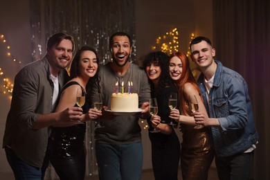 Happy friends with tasty cake and glasses of sparkling wine celebrating birthday indoors