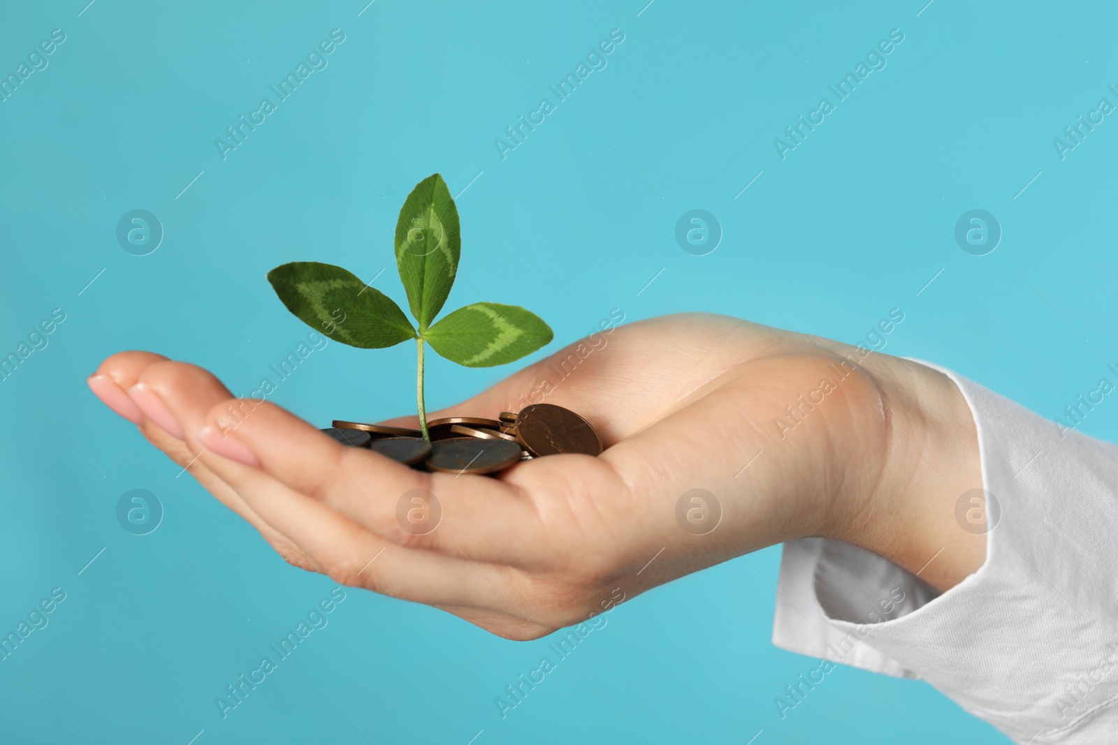 Photo of Woman holding coins with green sprout on turquoise background, closeup. Investment concept