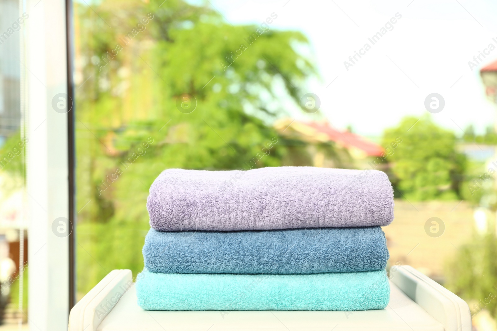 Photo of Stack of clean soft terry towels near window in room