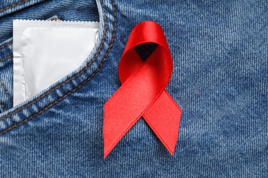 Photo of Jeans with red ribbon and condom, flat lay. AIDS disease awareness