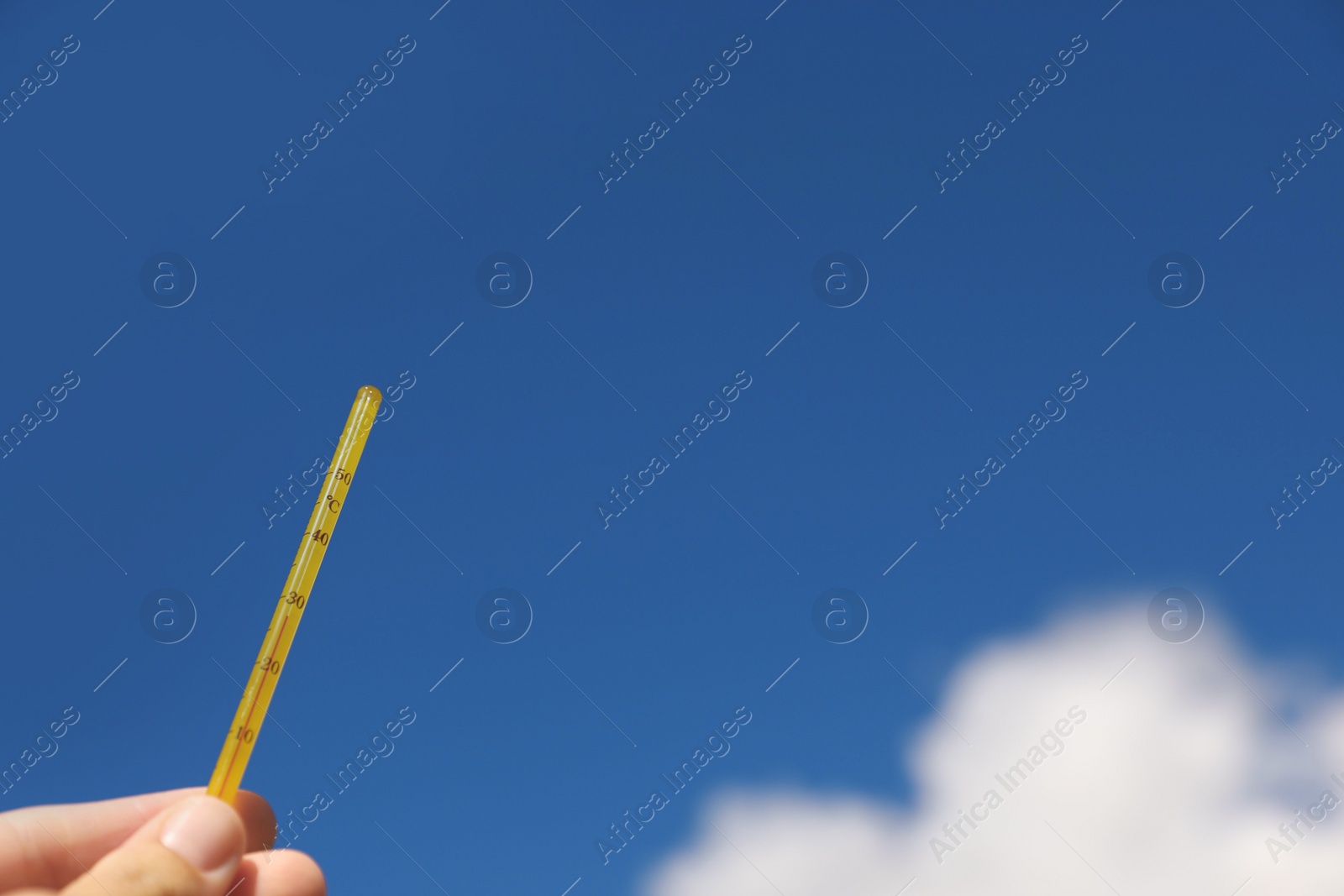 Photo of Woman holding weather thermometer against blue sky, closeup. Space for text