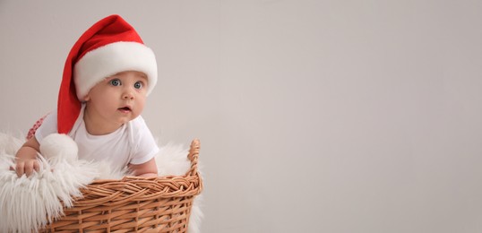 Image of Cute baby in wicker basket on light grey background, banner design with space for text. Christmas celebration