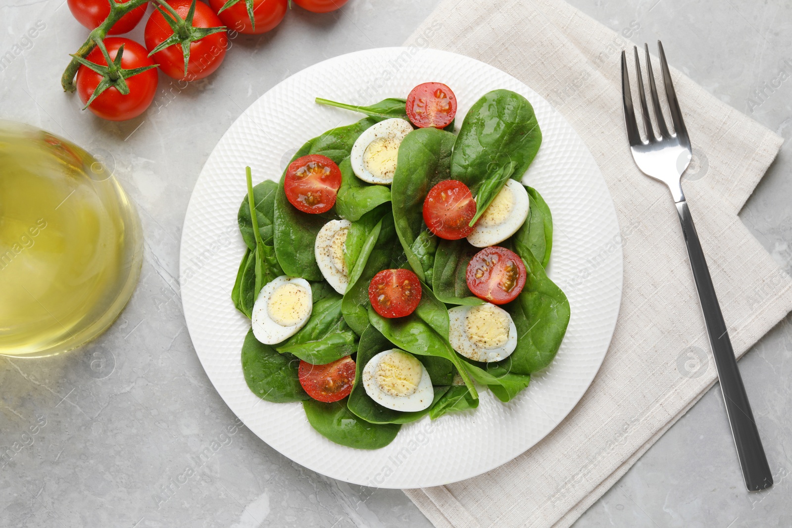 Photo of Delicious salad with boiled eggs, tomatoes and spinach served on light grey table, flat lay