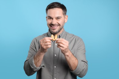 Photo of Happy man holding tasty fortune cookie with prediction on light blue background