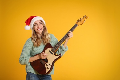 Photo of Young woman in Santa hat playing electric guitar on yellow background, space for text. Christmas music