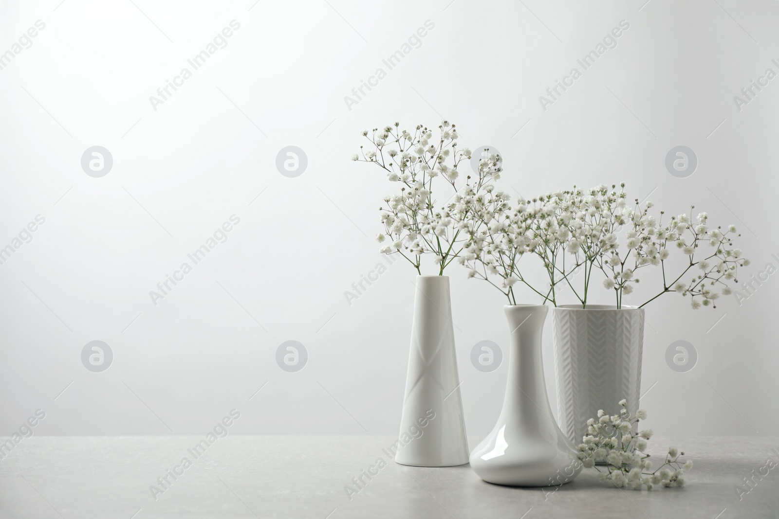 Photo of Gypsophila flowers in vases on table against white background. Space for text