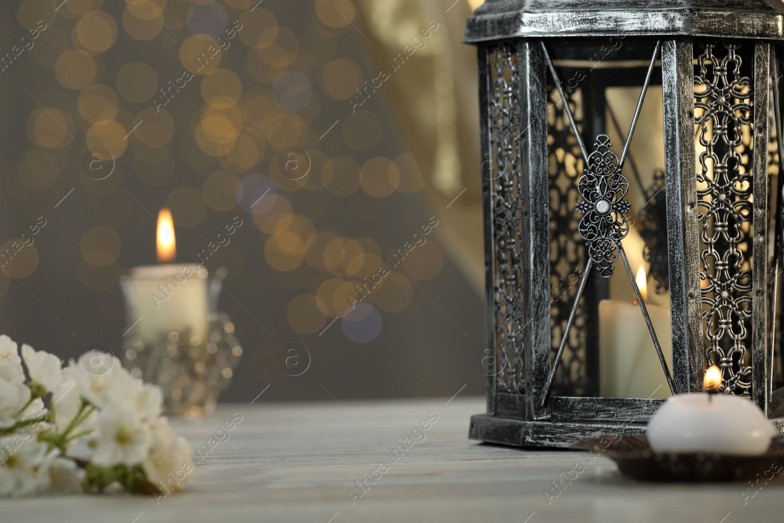 Photo of Arabic lantern and burning candles on table against blurred lights