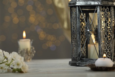 Photo of Arabic lantern and burning candles on table against blurred lights