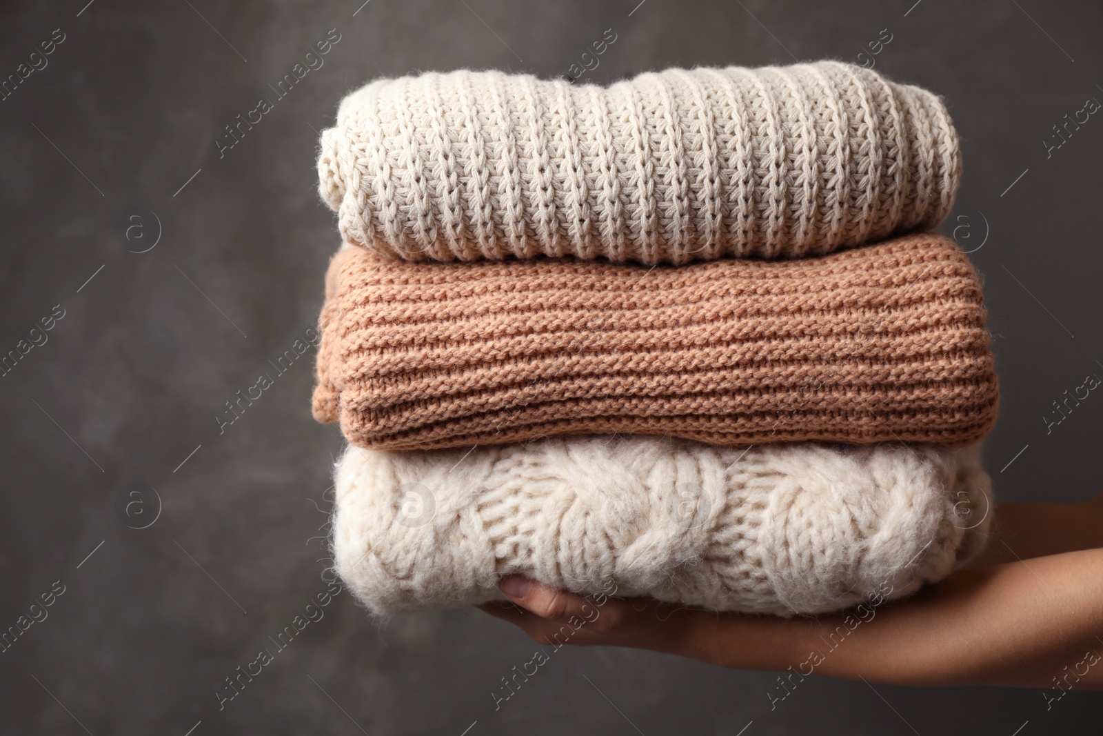 Photo of Woman holding stack of folded warm knitted sweaters against dark background