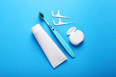 Photo of Container with dental floss, toothpaste and toothbrush on light blue background, flat lay