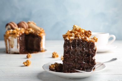 Photo of Piece of delicious homemade cake with caramel sauce and popcorn on table