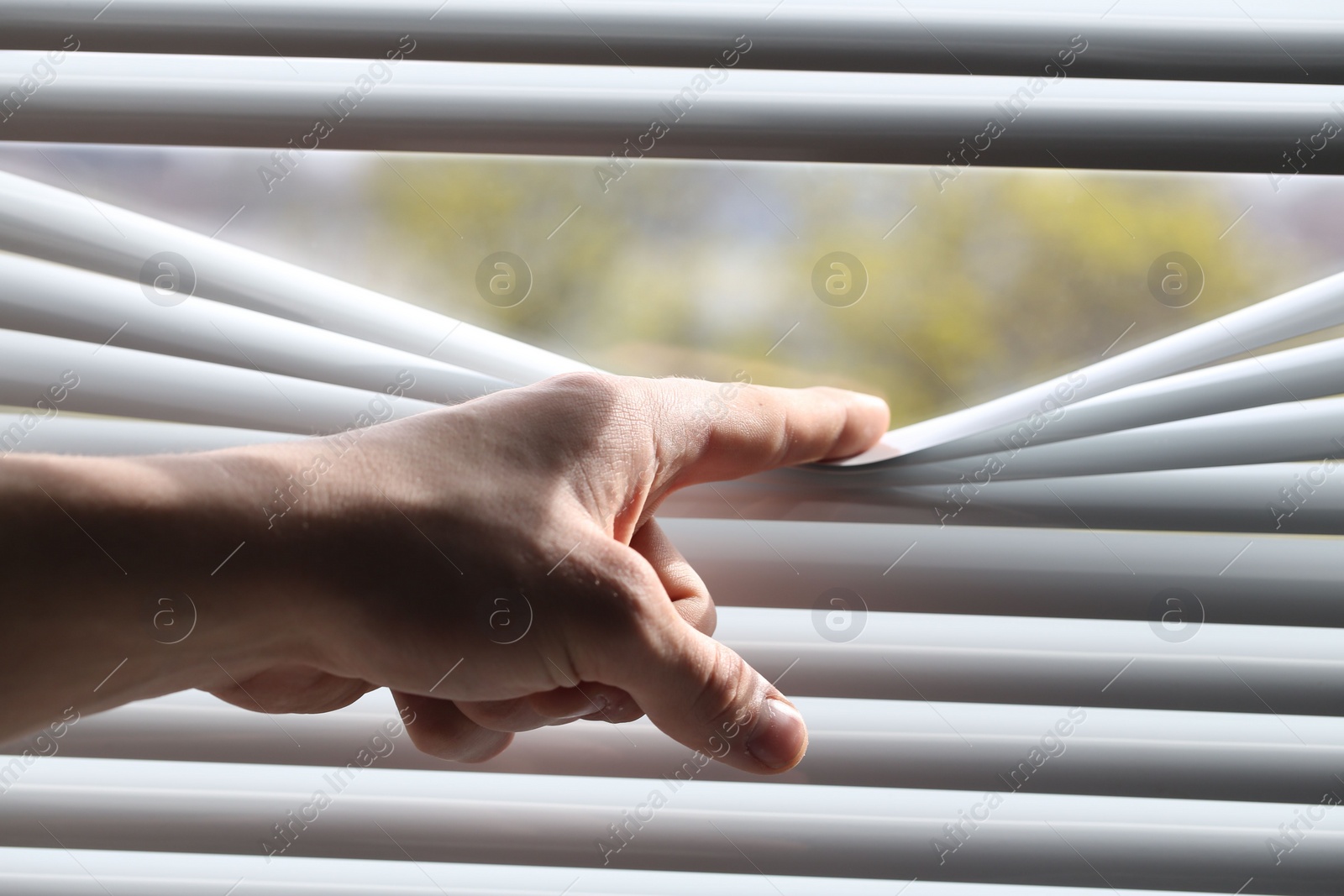 Photo of Man separating slats of white blinds indoors, closeup