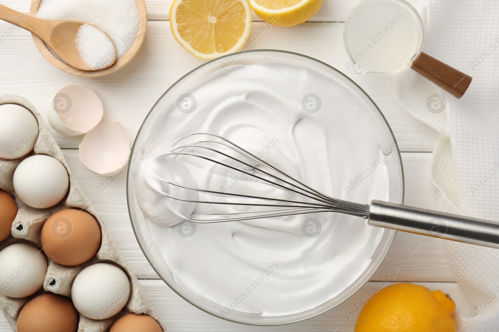 Photo of Bowl with whipped cream, whisk and ingredients on white wooden table, flat lay