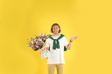 Young handsome man with beautiful flower bouquet on yellow background