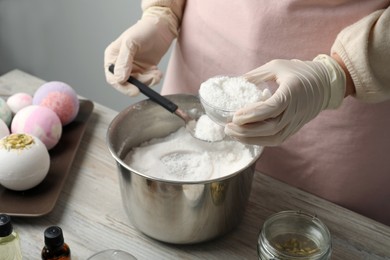 Photo of Woman in gloves making bath bomb at wooden table, closeup