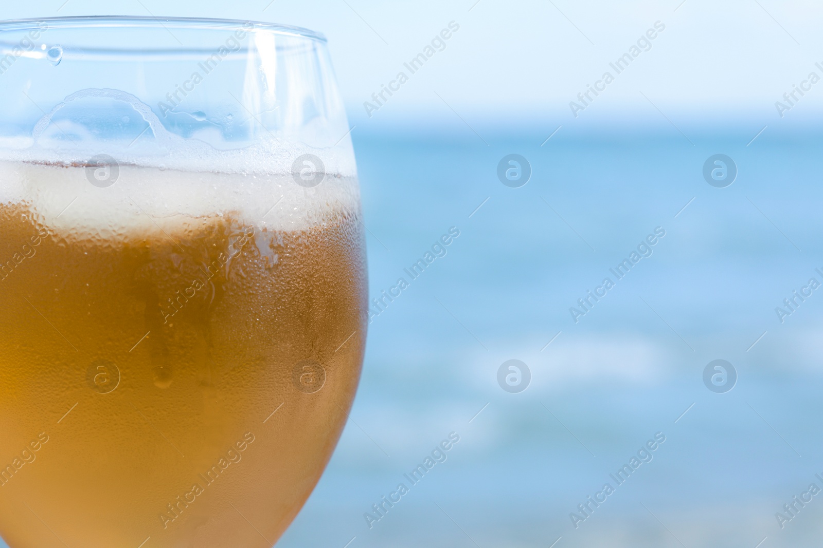 Photo of Cold beer in glass on beach, closeup. Space for text