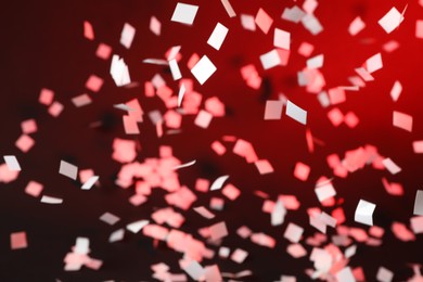 Photo of White confetti falling down on dark red background