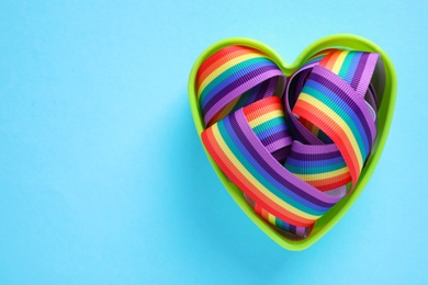 Heart shaped mold and bright rainbow ribbon on color background, top view with space for text. Symbol of gay community