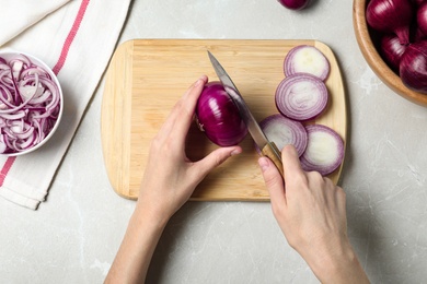 Photo of Woman cutting fresh red onion on wooden board at light marble table, top view