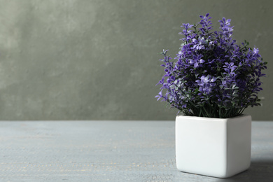 Photo of Artificial plant in white flower pot on grey wooden table. Space for text