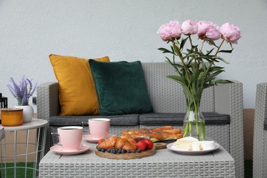 Photo of Morning drink, pastry, berries, cheese and vase with flowers on rattan table. Summer breakfast on terrace