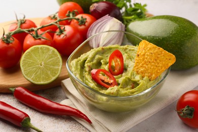 Photo of Bowl of delicious guacamole, nachos chip and ingredients on table, closeup