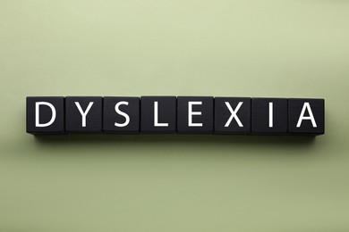 Wooden cubes with word Dyslexia on olive background, flat lay