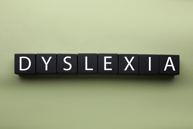 Photo of Wooden cubes with word Dyslexia on olive background, flat lay