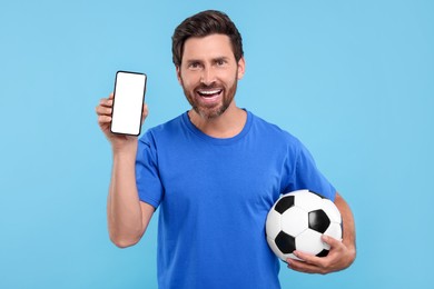 Photo of Happy sports fan with soccer ball and smartphone on light blue background
