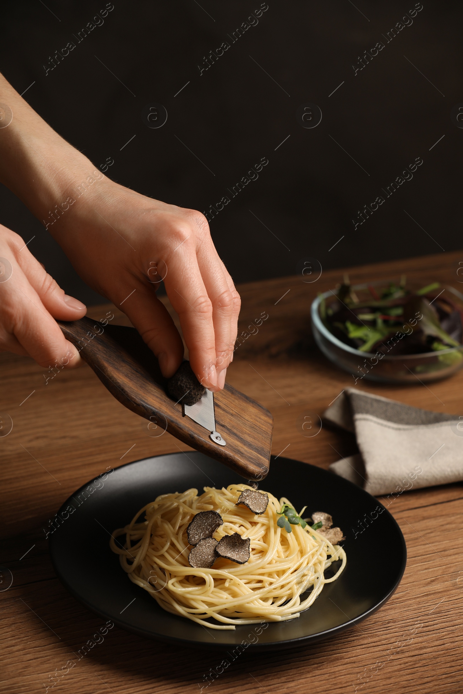 Photo of Woman slicing truffle onto spaghetti at wooden table, closeup