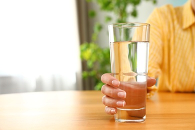 Photo of Woman holding glass of water at wooden table, closeup with space for text. Refreshing drink