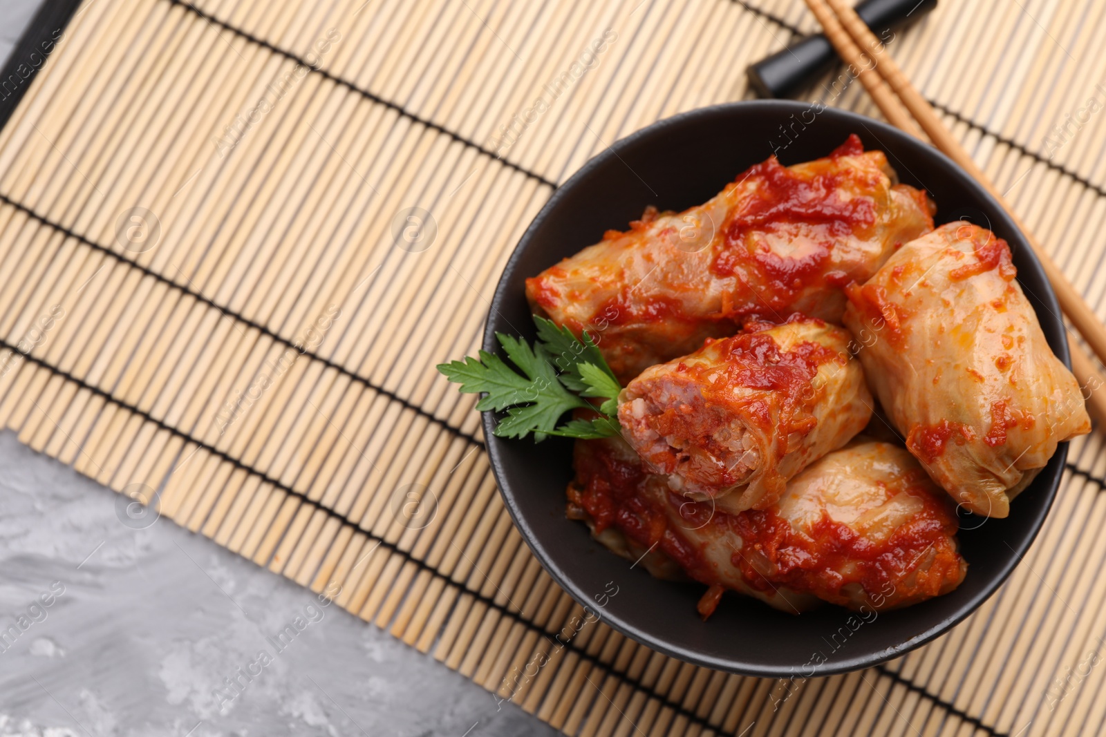 Photo of Delicious stuffed cabbage rolls cooked with tomato sauce on grey table, top view. Space for text