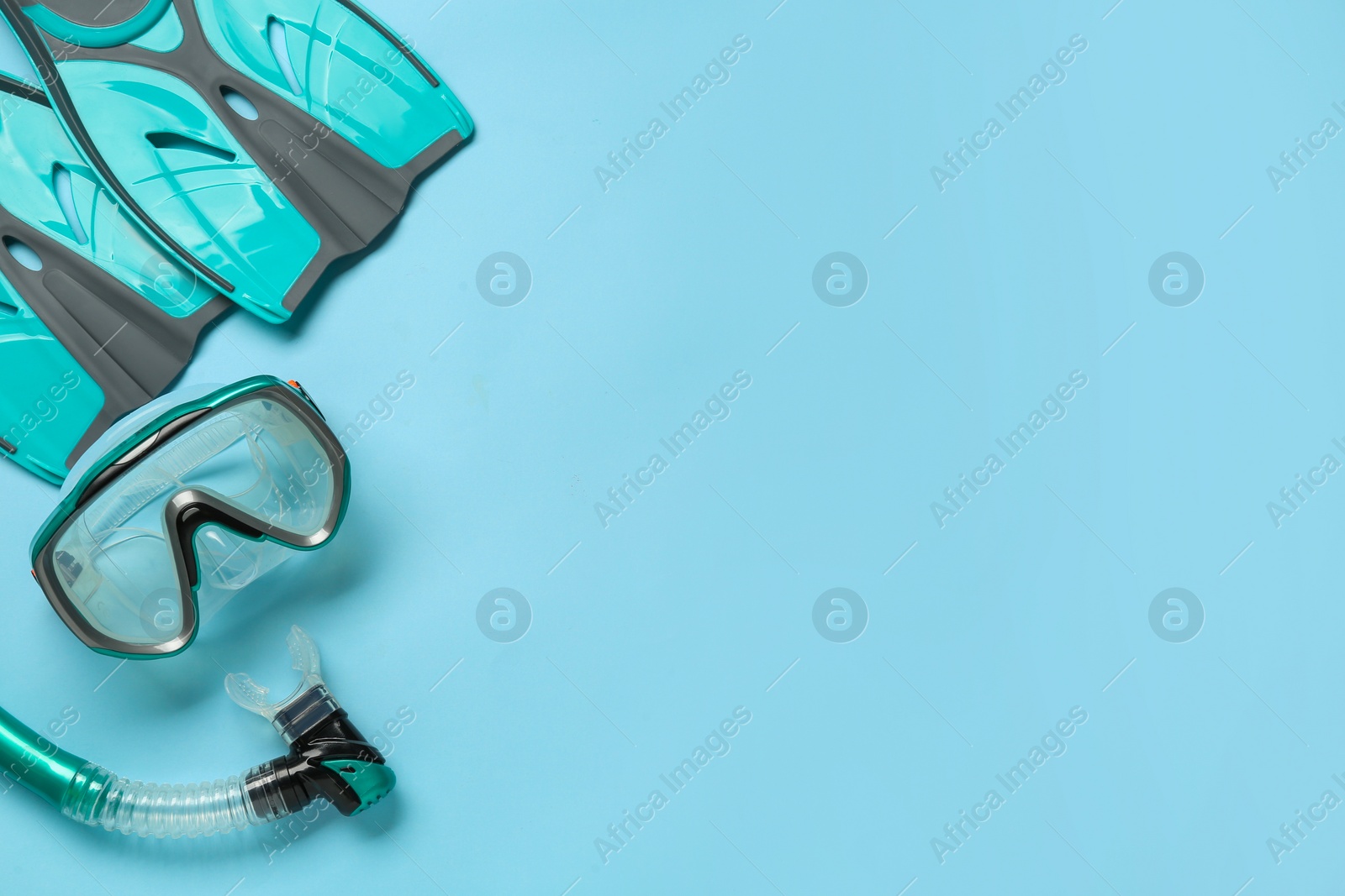 Photo of Pair of turquoise flippers and mask on light blue background, flat lay. Space for text