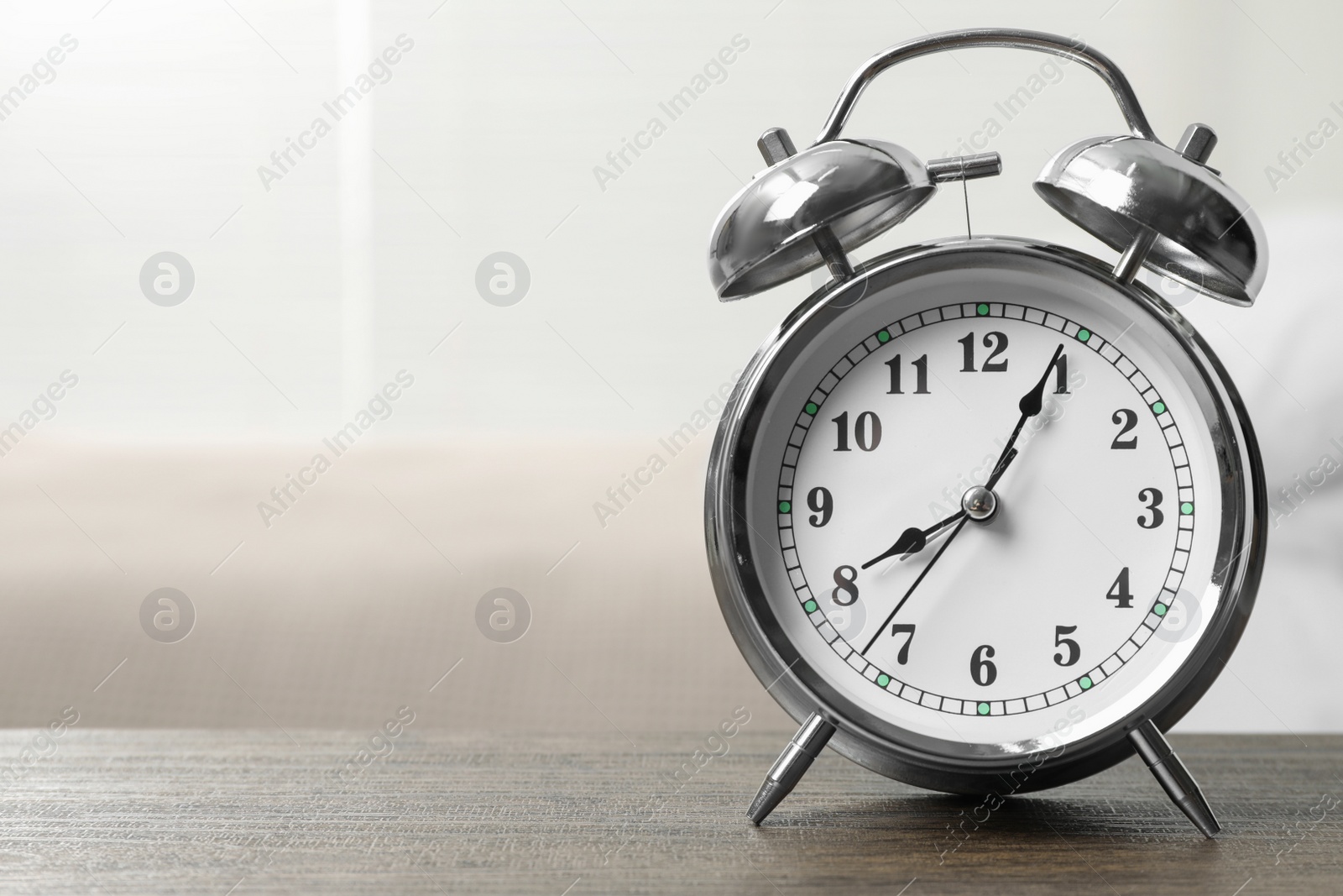 Photo of Silver alarm clock on wooden table in bedroom, space for text