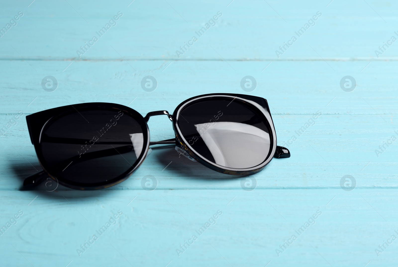 Photo of Stylish sunglasses on blue wooden background. Fashionable accessory