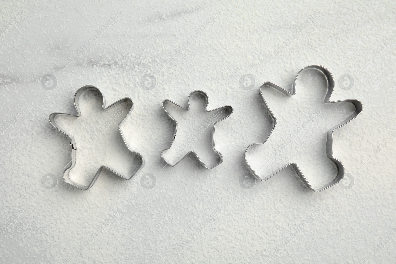 Photo of Gingerbread man cookie cutters and flour on white marble table, flat lay