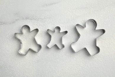 Gingerbread man cookie cutters and flour on white marble table, flat lay