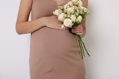 Photo of Pregnant woman in beige dress with bouquet of roses on white background, closeup