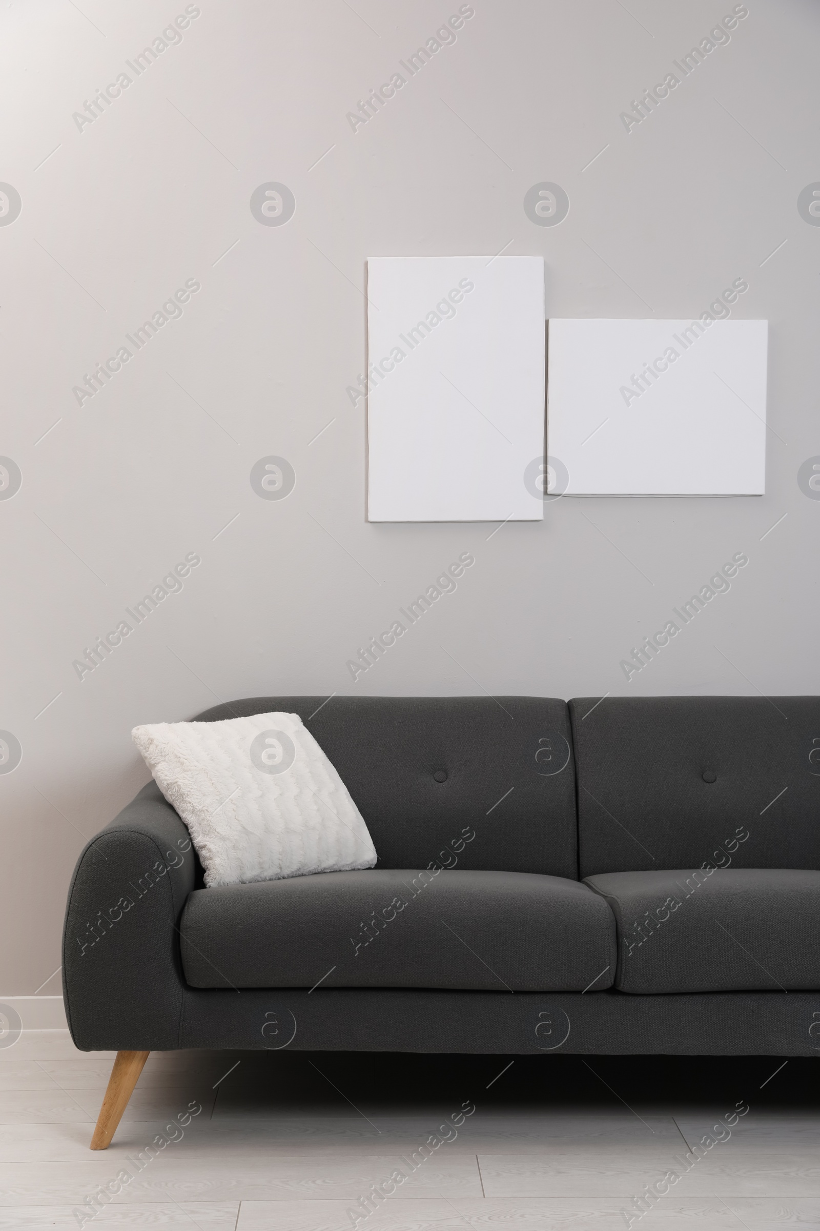 Photo of Blank canvas on wall over comfortable sofa indoors. Space for design