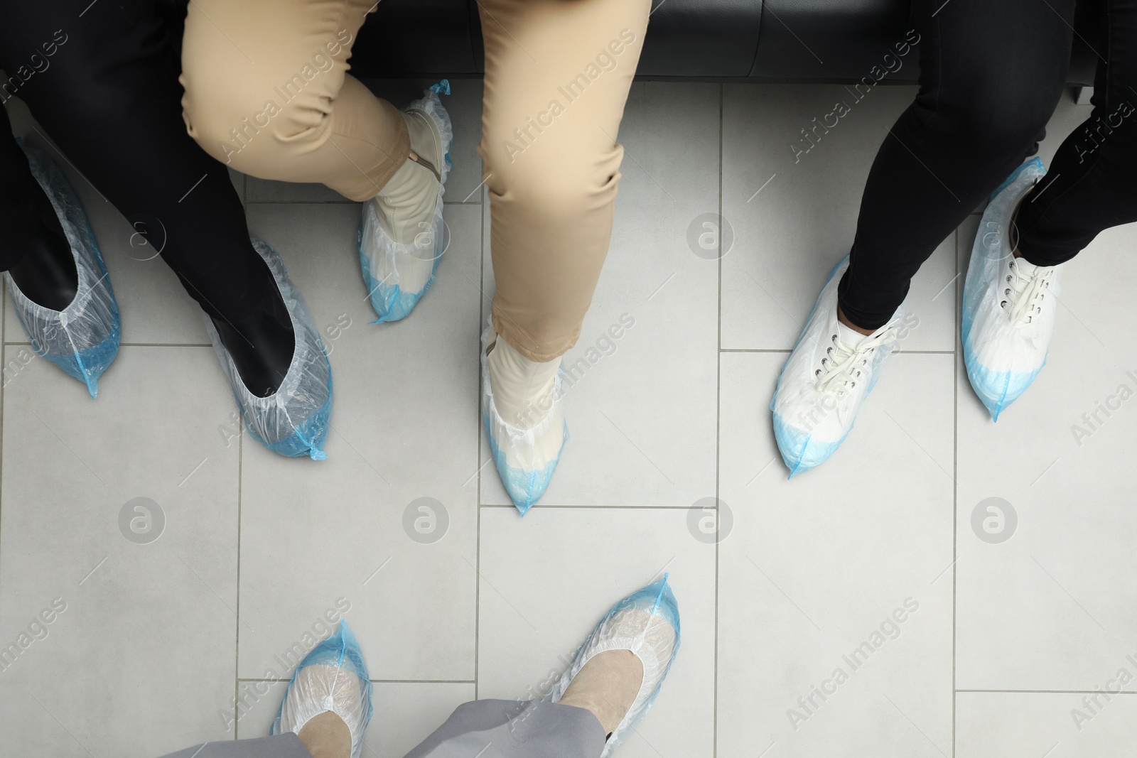 Photo of Women wearing blue shoe covers onto different footwear indoors, top view