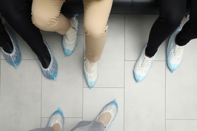 Women wearing blue shoe covers onto different footwear indoors, top view