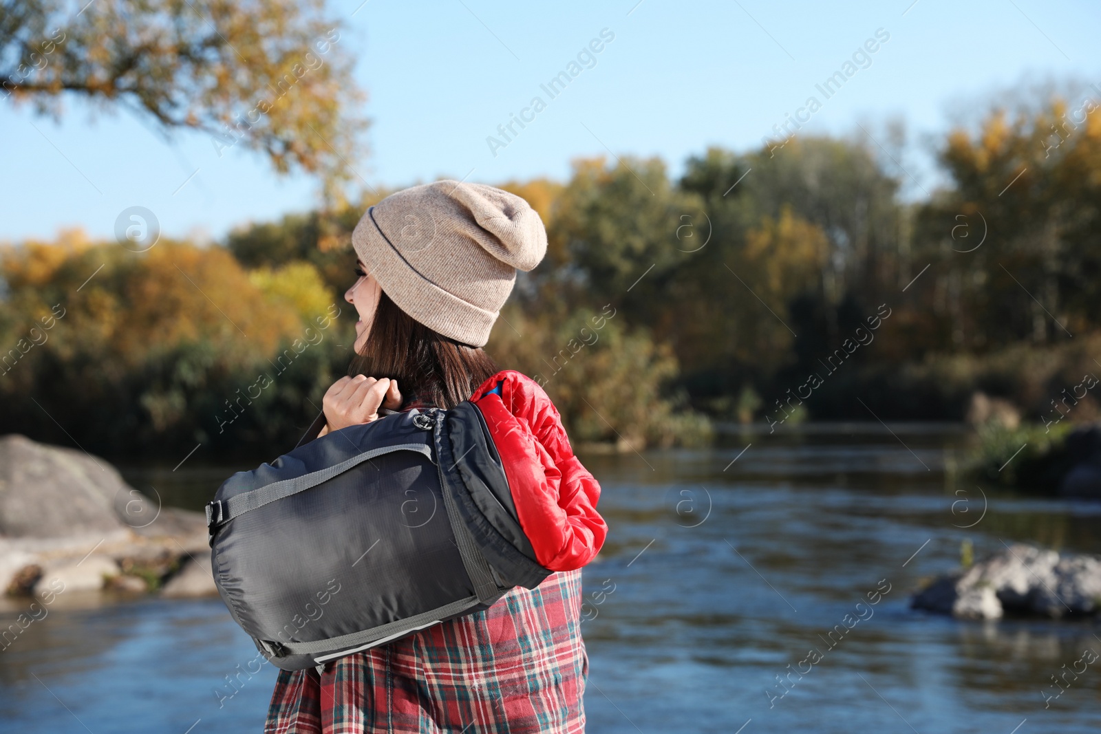Photo of Female camper with sleeping bag near pond. Space for text