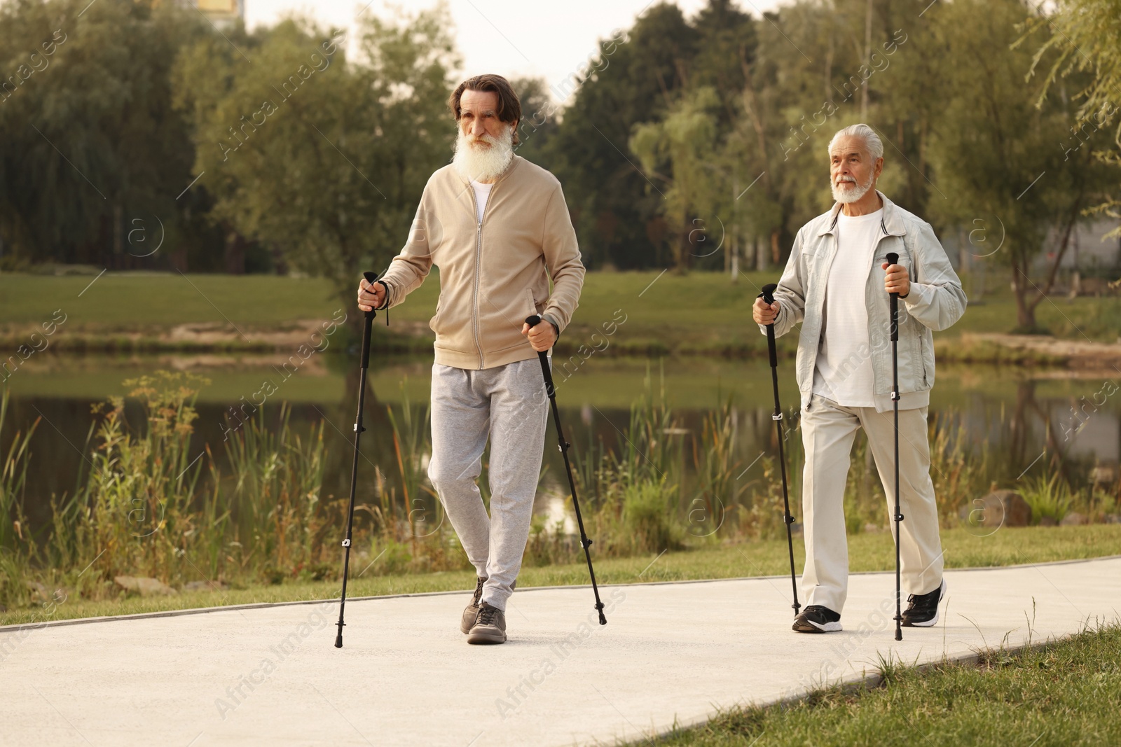 Photo of Two senior friends performing Nordic walking outdoors