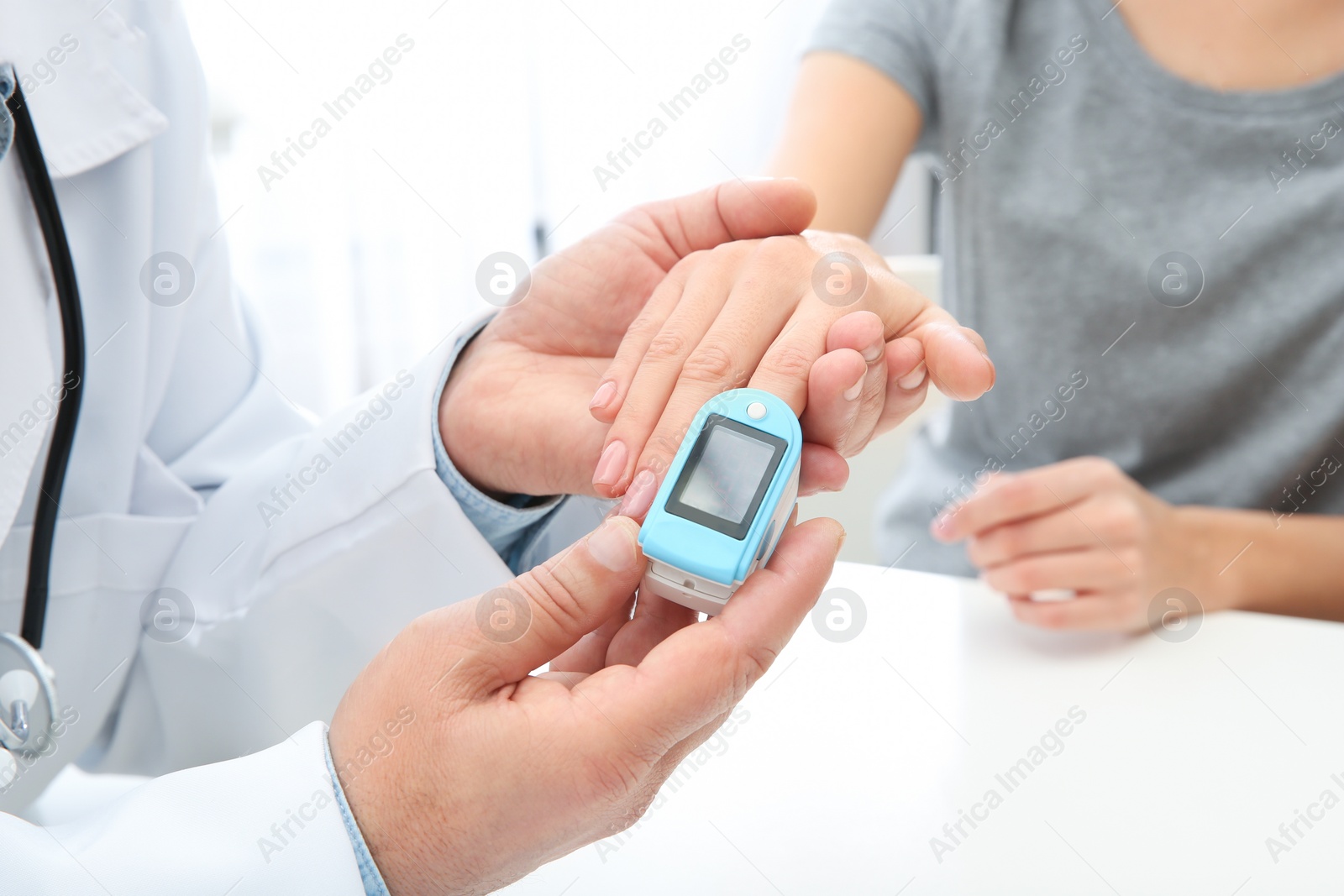 Photo of Doctor checking young woman's pulse with medical device at table in hospital, closeup