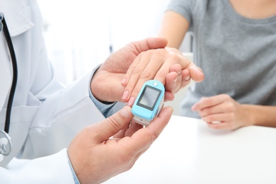 Doctor checking young woman's pulse with medical device at table in hospital, closeup