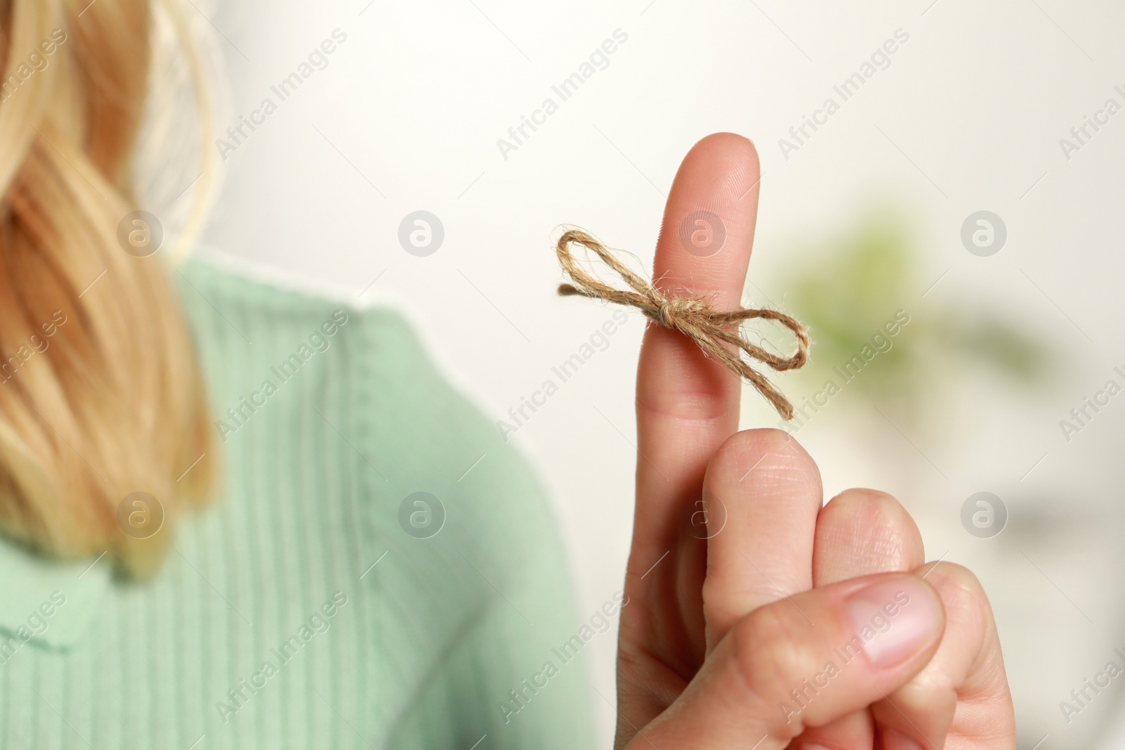 Photo of Woman showing index finger with tied bow as reminder on blurred background, closeup